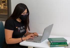 Estudiante sentada en escritorio, escribiendo en computadora